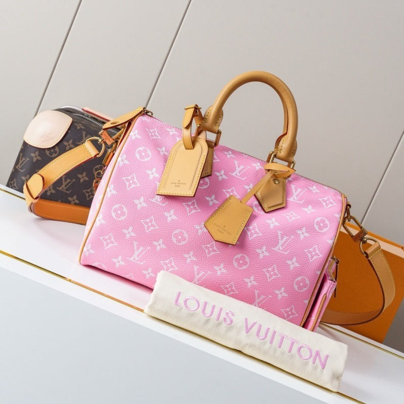 A pink Louis Vuitton monogram Speedy handbag with tan leather handles and tags, displayed on a white shelf alongside a cream dust bag and other bags in the background.