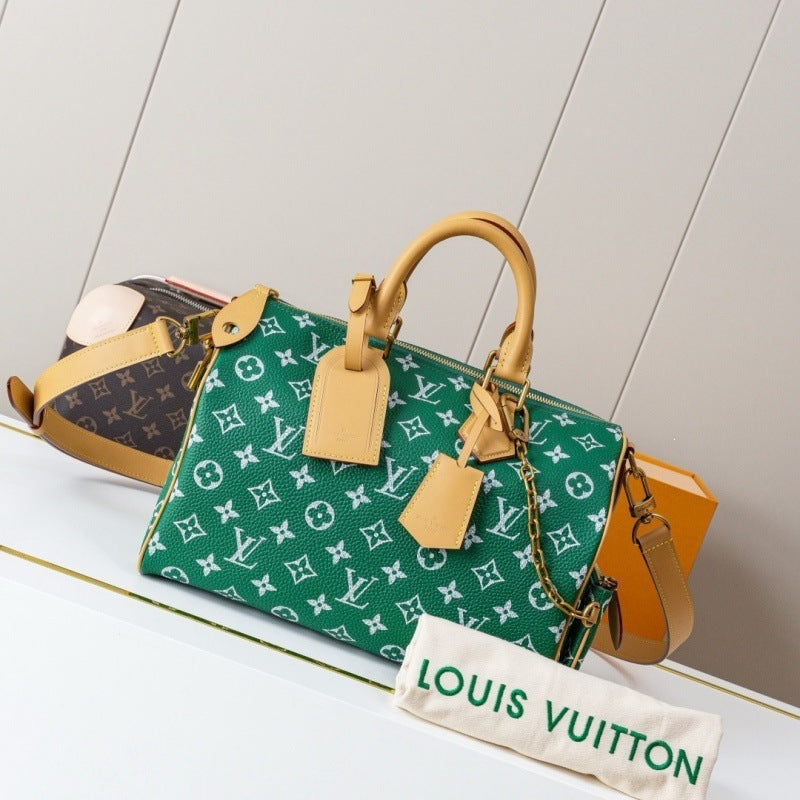 A green Louis Vuitton monogram Speedy handbag with tan leather handles and trim, displayed on a white surface with a Louis Vuitton dust bag in front and another bag partially visible behind it.