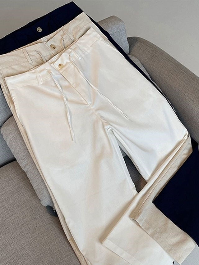 Cream-colored wide-leg drawstring pants laid flat on a gray sofa, with navy blue folded fabric pieces placed underneath for styling. A Chinese watermark is visible in the bottom right corner.