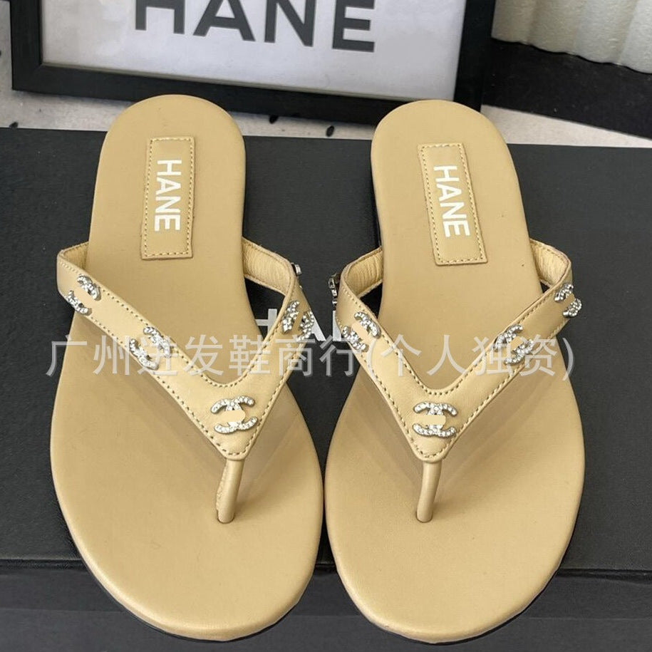 A pair of beige flat thong sandals with rhinestone-embellished straps, featuring a HANE brand insole, displayed on a dark surface.