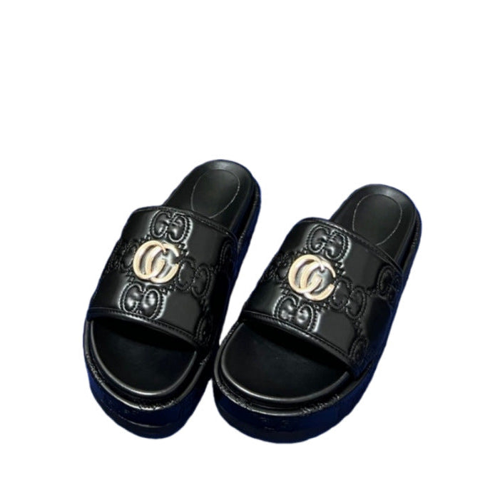 A pair of black platform slide sandals featuring embossed GG monogram patterns and a prominent gold-tone interlocking GG logo on the strap, set against a plain white background.