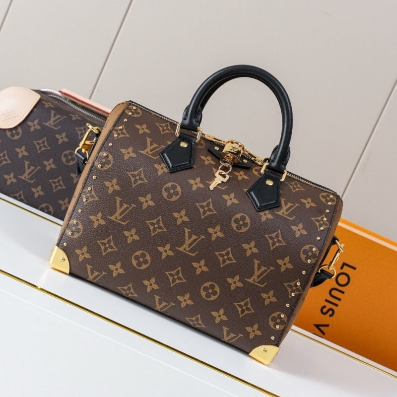 Louis Vuitton monogram canvas handbag with black leather top handle and trim, gold-tone hardware, and gold corner protectors, displayed on a white surface with an orange Louis Vuitton box partially visible.
