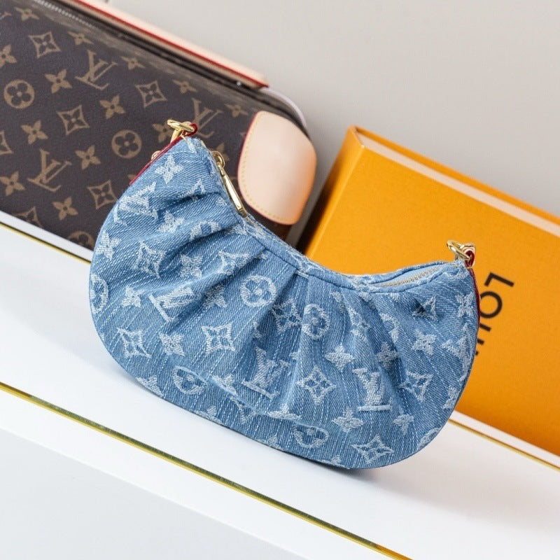 A blue monogrammed fabric pouch with gold-tone hardware, styled on a white surface next to a Louis Vuitton monogram bag and an orange Louis Vuitton box.