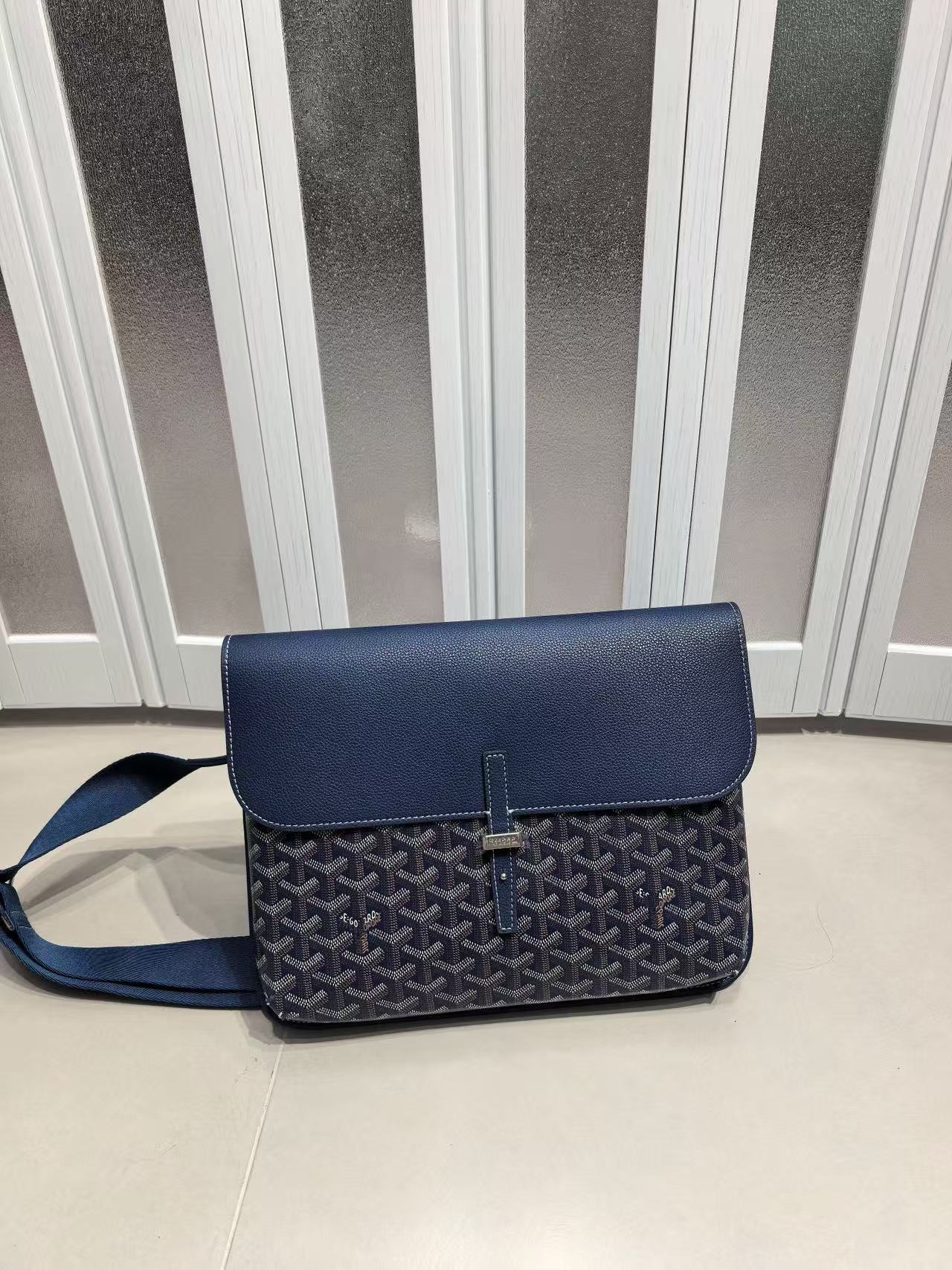 Blue textured handbag on a light-colored floor with a striped wall in the background