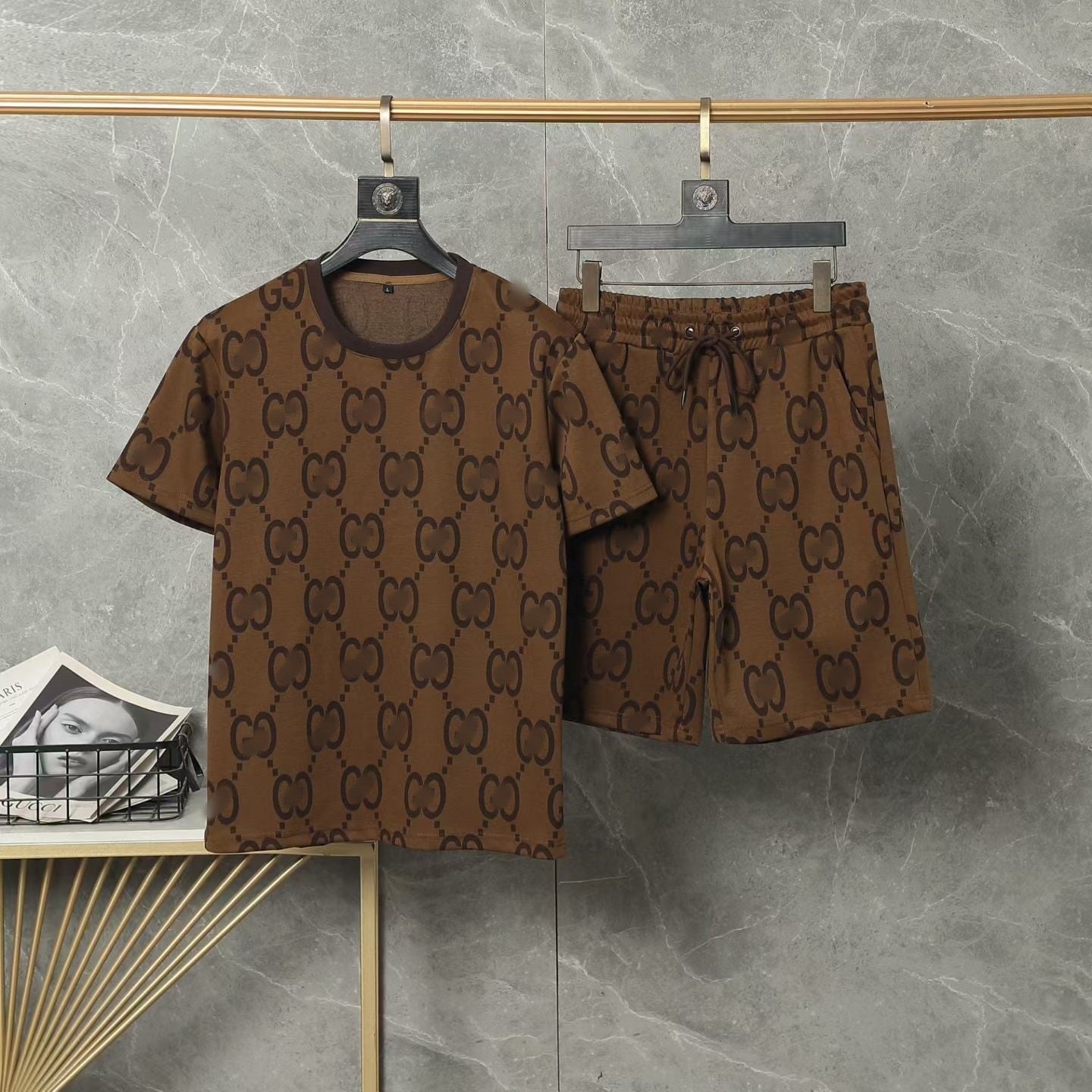 Brown patterned shirt and shorts set hanging on a rack against a gray marble wall.