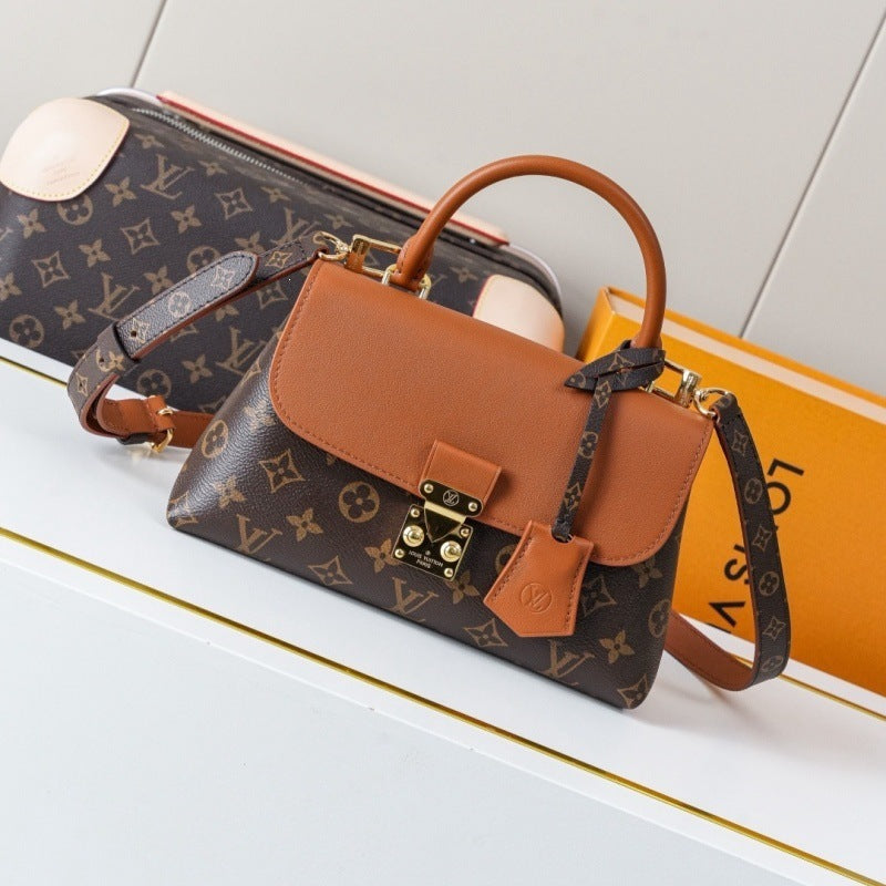 A Louis Vuitton handbag in brown monogram canvas with tan leather trim and a top handle, styled on a white surface with a matching pouch and orange Louis Vuitton box in the background.