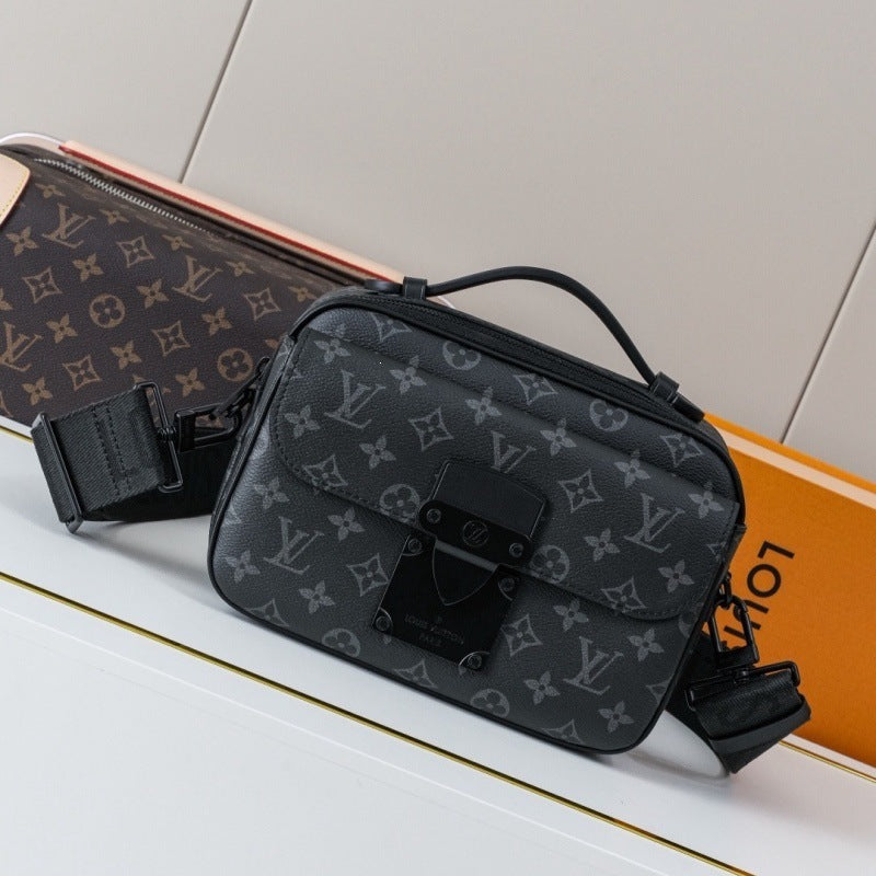 A Louis Vuitton monogram shoulder bag in black coated canvas with a black leather top handle and front flap closure, displayed on a white surface with a Louis Vuitton monogram pouch and orange box in the background.