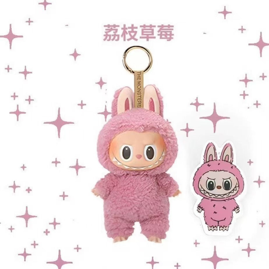 A pink plush character keychain with a gold metal ring and a small matching sticker shown beside it on a white background with pink star accents. The keychain character wears a fuzzy pink bunny-style outfit, and the sticker shows the same design.