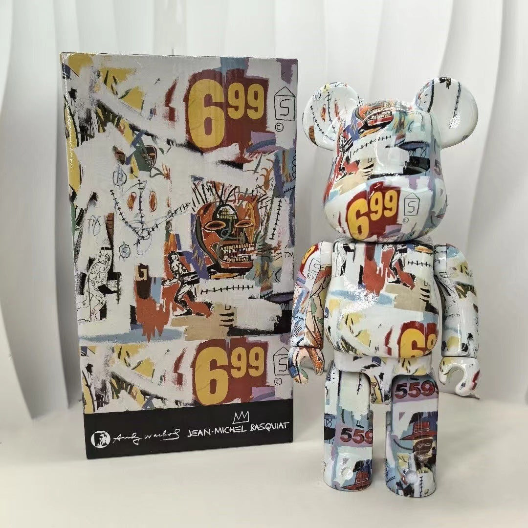 A collectible bear figure and its original box, both decorated with a colorful graffiti-style collage print featuring the number 699. The figure is posed next to its packaging on a white surface against a white curtain background.