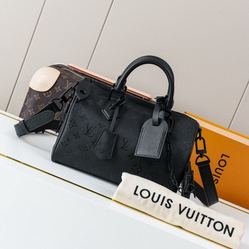 A black Louis Vuitton monogram handbag displayed on a white surface with a Louis Vuitton dust bag and orange box in the background.
