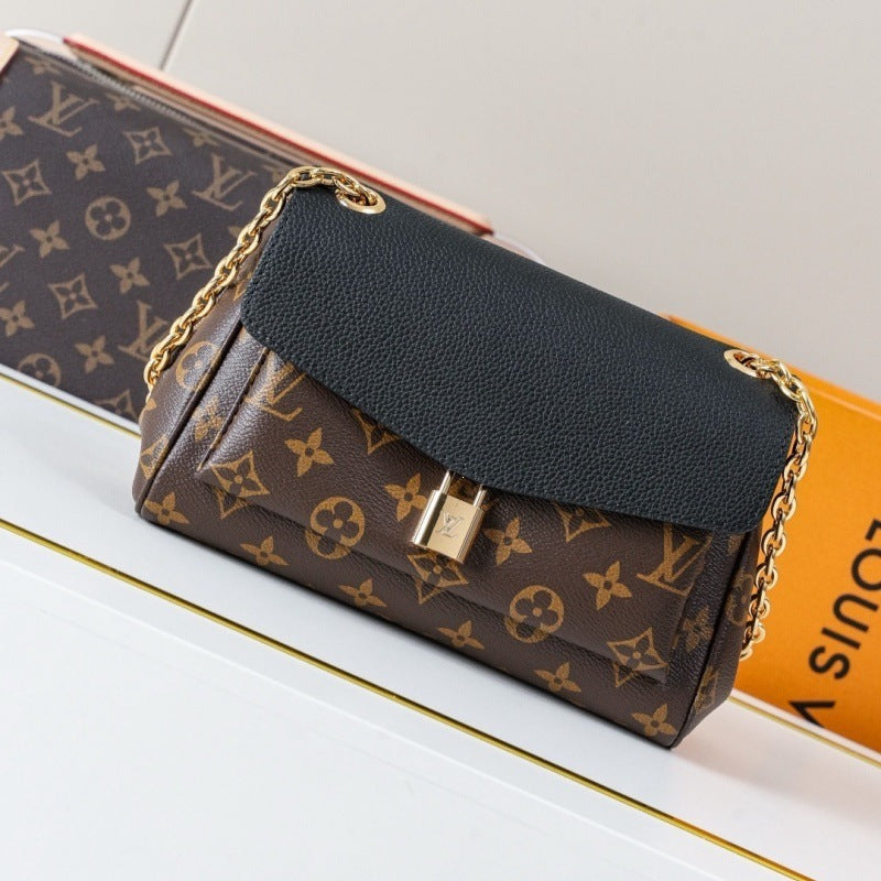 A Louis Vuitton monogram shoulder bag with a black pebbled leather flap and gold-tone chain strap, resting on a white surface next to its orange packaging box.
