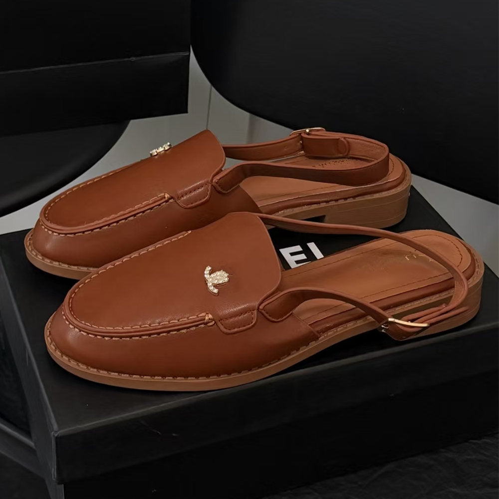 A pair of brown leather slingback loafers with a small gold bee logo on the toe, displayed on a black shoebox.