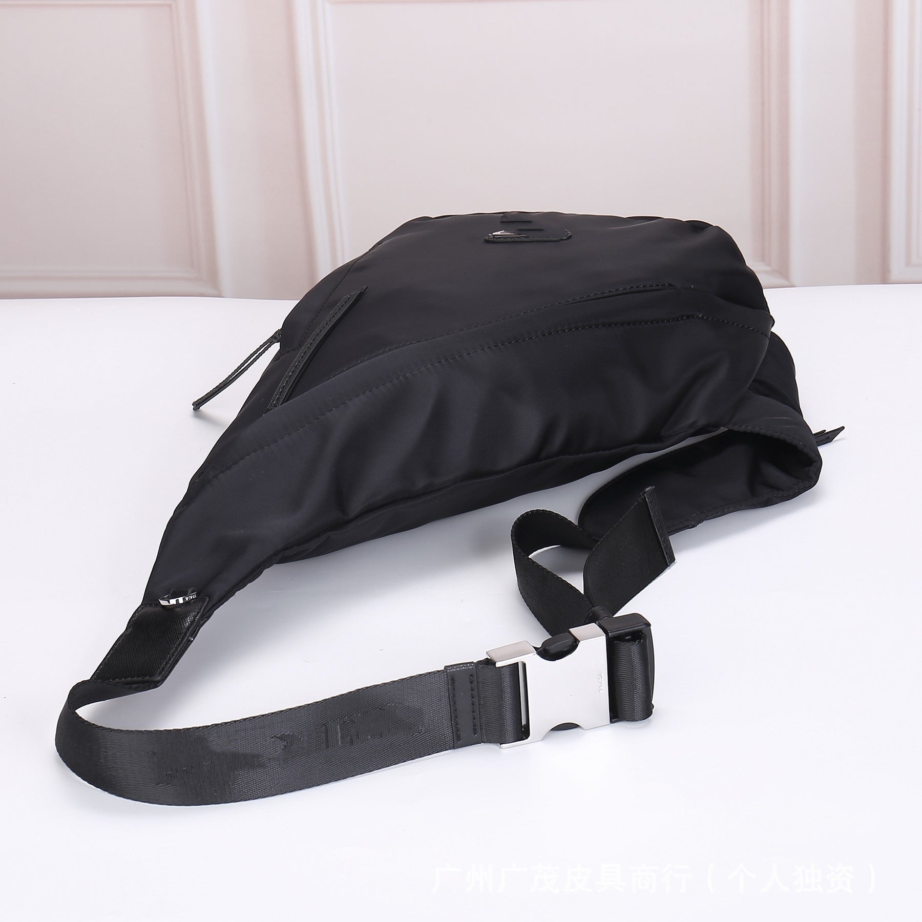 Black Prada waist bag on a white surface with a light-colored wall background