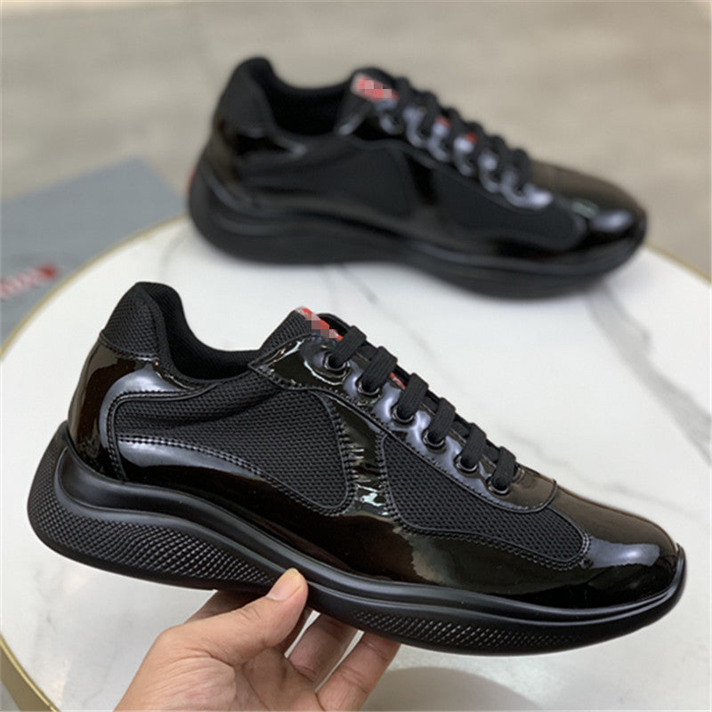 Black sneakers with a glossy finish held by a hand on a light background