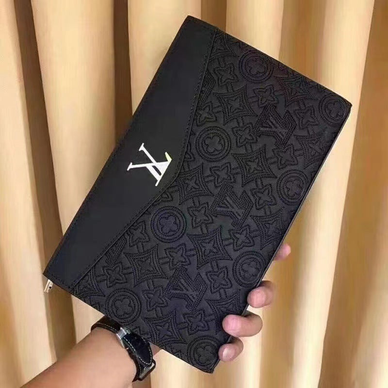 A black embossed monogram clutch or wallet with a silver-tone LV monogram logo, held by a hand in front of beige curtains.