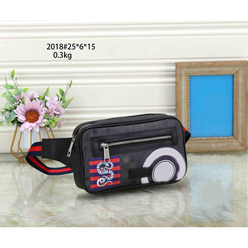 A black waist bag with a red and blue striped strap, featuring a Pokémon logo patch and a circular Pokémon ball graphic, displayed on a reflective surface with decorative props.