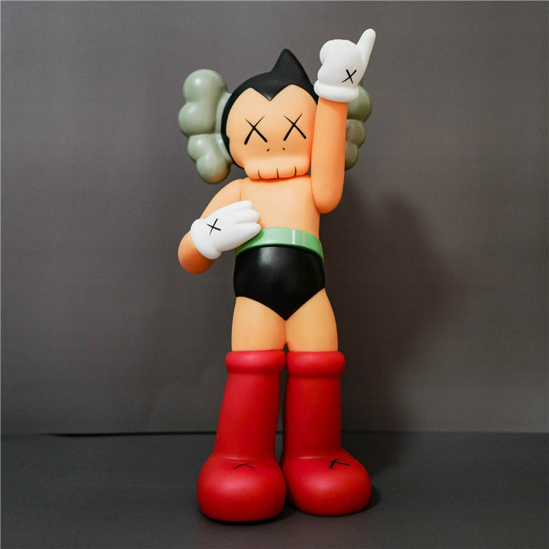 A stylized collectible figure of a cartoon character with black hair, gray hair tufts, a peach face, black shorts, a green waistband, and red boots, posed against a dark gray studio background.