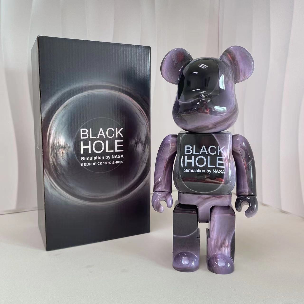 A translucent purple bear-shaped collectible figure stands next to its black retail box on a light surface. The box features a large circular black-hole graphic with the text 'BLACK HOLE Simulation by NASA'.