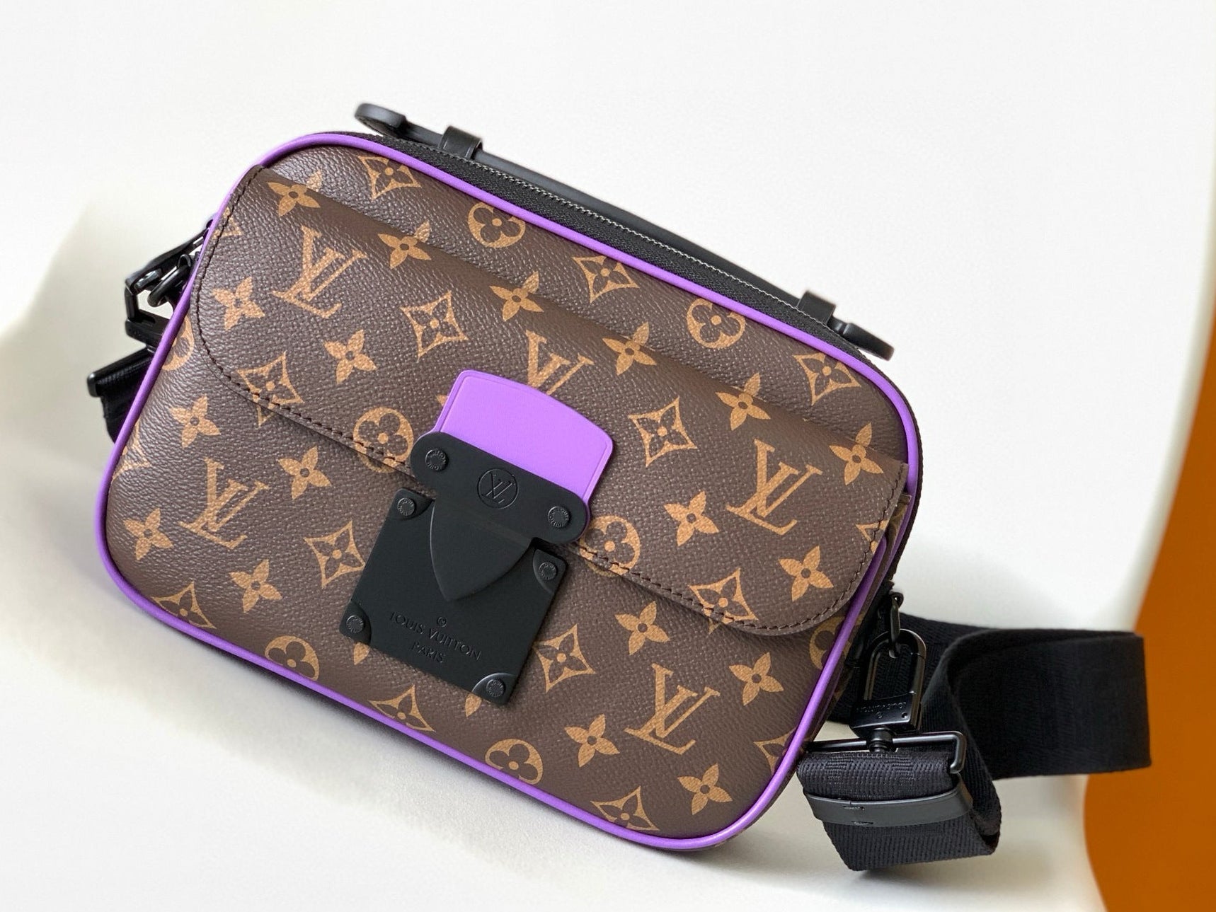 Designer handbag with monogram pattern and purple accents on a white background