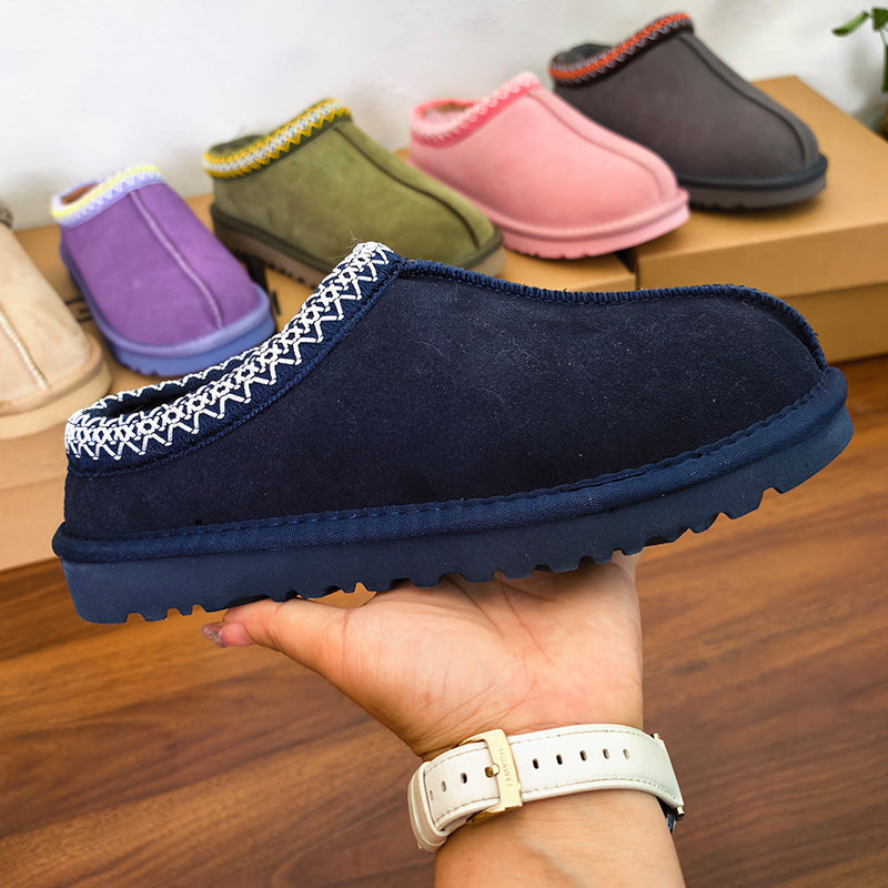 Navy blue slipper held in a hand with other colored slippers in the background.
