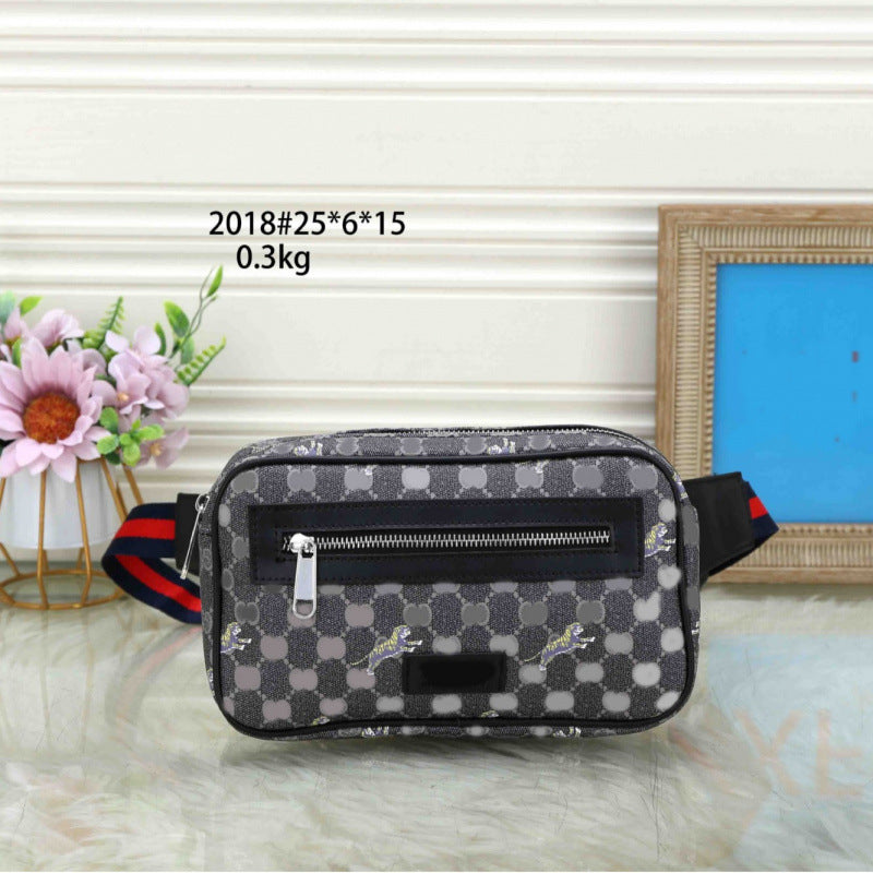 A men's crossbody belt bag with a gray and black checkerboard pattern, featuring a front zippered pocket and a red and blue striped webbing strap. The bag is displayed on a white marble surface with decorative props, including a vase of pink flowers and a picture frame, against a white paneled wall.