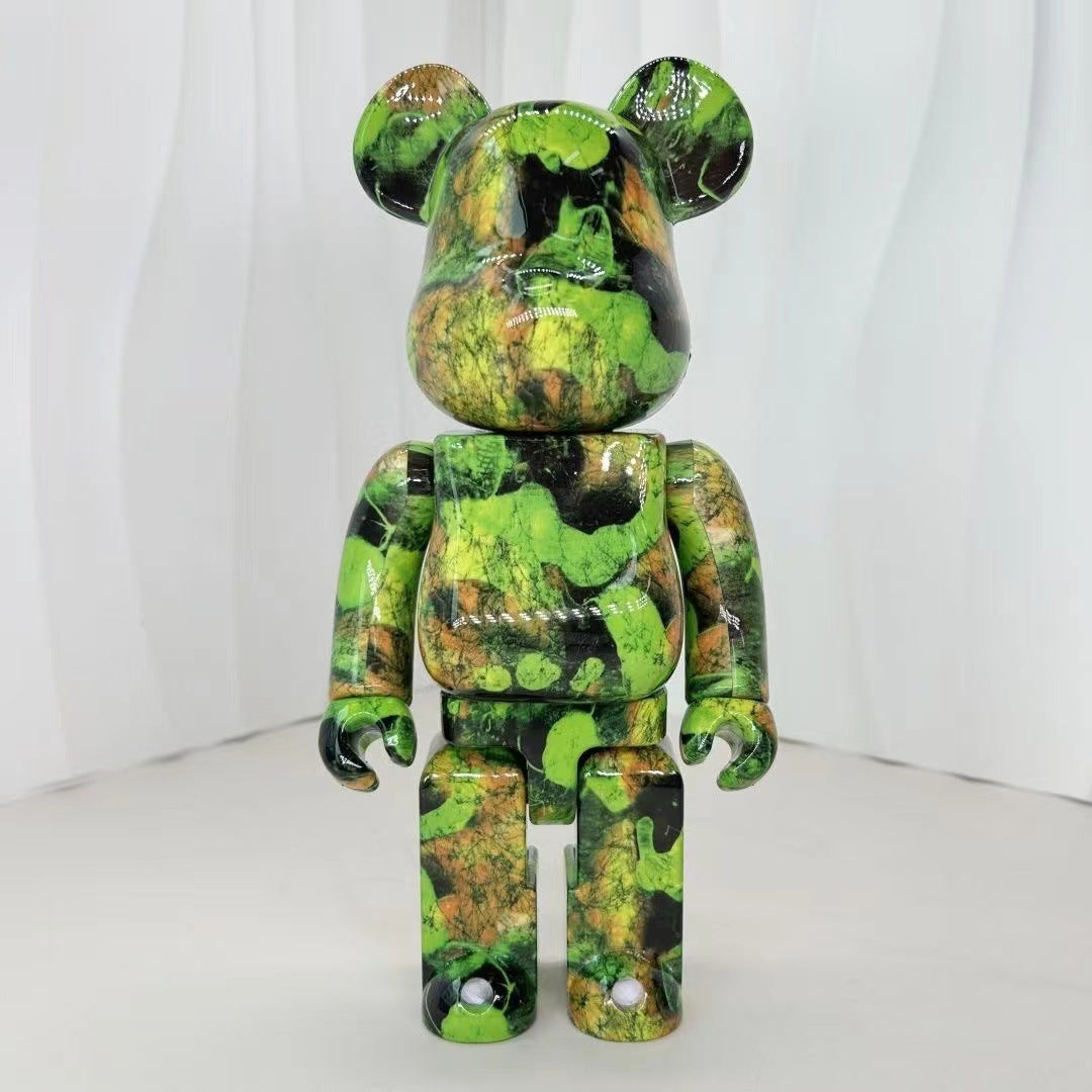 A collectible bear-shaped figure with a glossy green, black, and brown marbled camouflage pattern, standing against a white draped background.