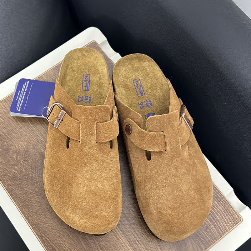 Pair of tan suede clogs with a tag on a wooden surface