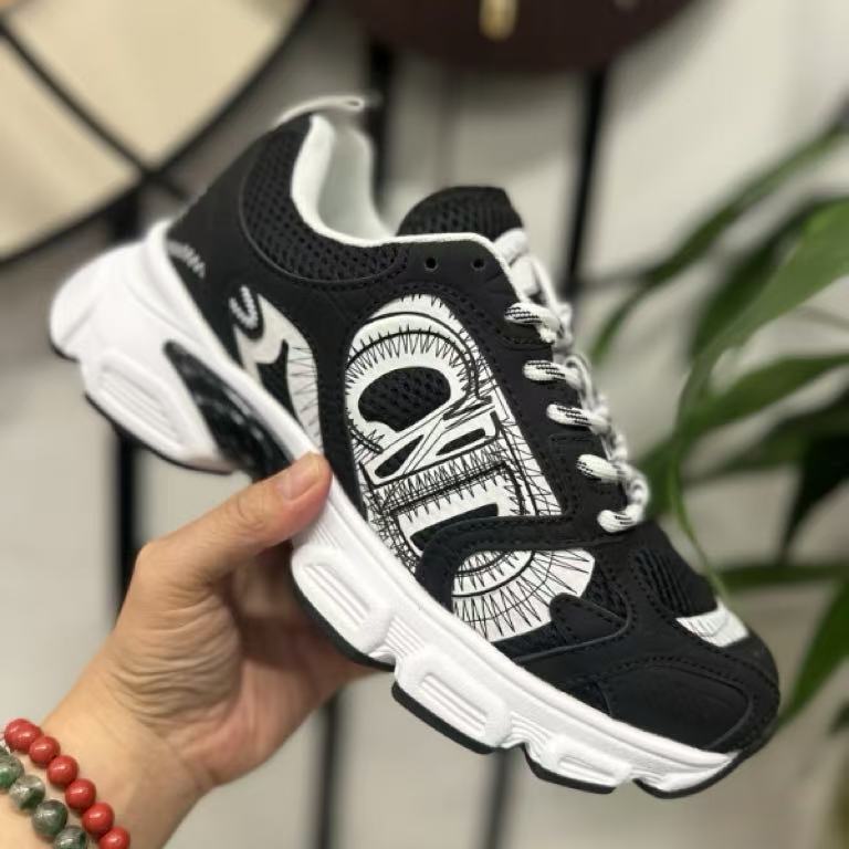 Black and white sneaker with detailed design held by a hand against a neutral background