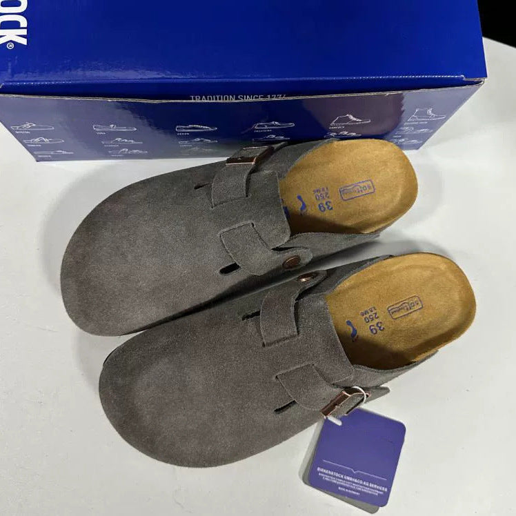 Pair of gray suede shoes with wooden soles on a white surface, with a blue box in the background.