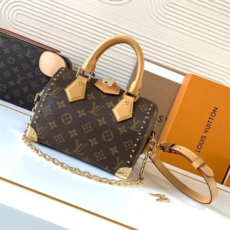 Louis Vuitton monogram canvas handbag with tan leather handles and trim, gold-tone chain strap, studded corners, and a Louis Vuitton box beside it on a white surface.