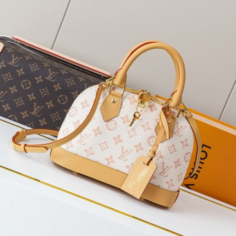 A Louis Vuitton handbag with a white and beige monogram pattern, tan leather trim, and gold-tone hardware, displayed on a white surface with a Louis Vuitton monogram pouch and orange box in the background.