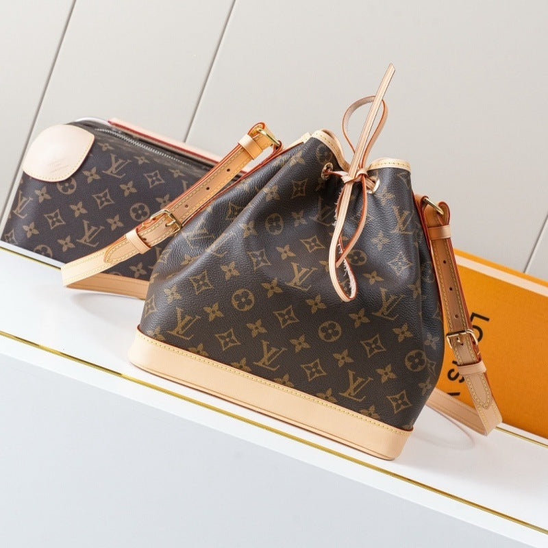 Louis Vuitton monogram canvas bucket bag with tan leather trim and drawstring closure, displayed on a white surface with a matching bag and orange box in the background.