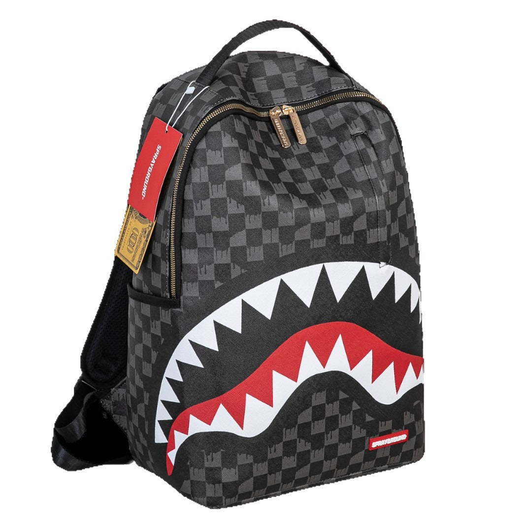 A Spraycraft Shark backpack in black and gray checkerboard pattern, featuring a large shark mouth graphic with white and red teeth on the front, a top handle, and a red brand tag.