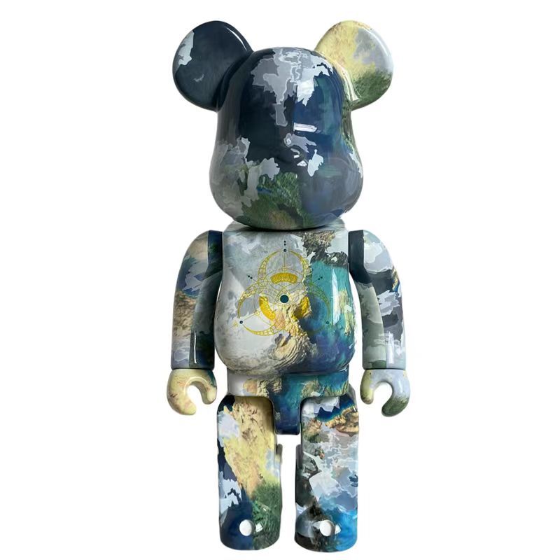 A bear-shaped collectible figure with a distressed, abstract art print in shades of blue, gray, green, and yellow, featuring a gold biohazard symbol on its chest, set against a plain white background.