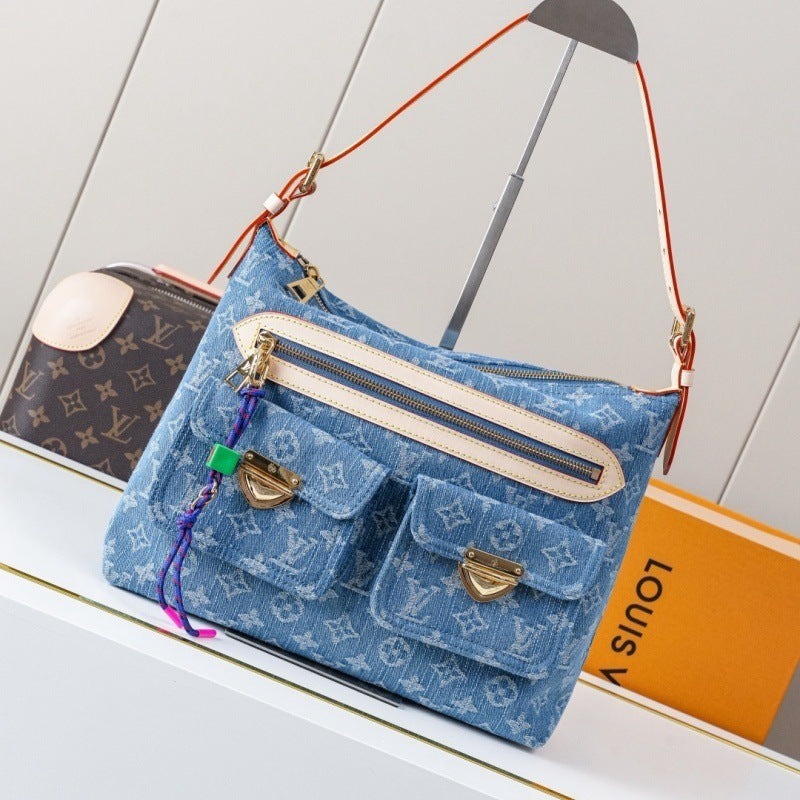 A blue Louis Vuitton monogram canvas shoulder bag with cream trim and gold-tone hardware, displayed on a white shelf next to a Louis Vuitton box and another monogram bag.