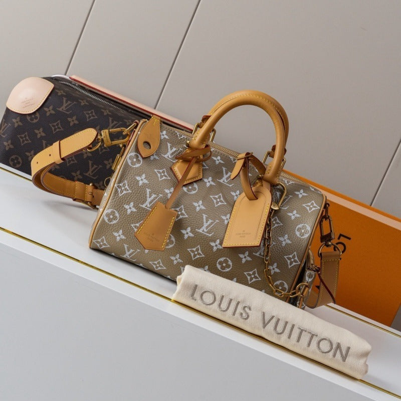 A Louis Vuitton monogram handbag in beige canvas with tan leather handles and tags, displayed on a white shelf with a dust bag and other bags in the background.