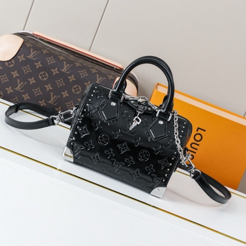 A black Louis Vuitton mini top-handle handbag with embossed monogram pattern and silver-tone hardware, displayed on a white surface with a matching monogram pouch and orange Louis Vuitton box in the background.