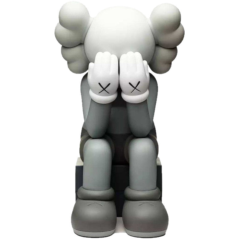 A gray and white KAWS-style seated figure with its hands over its face, shown against a plain white background.