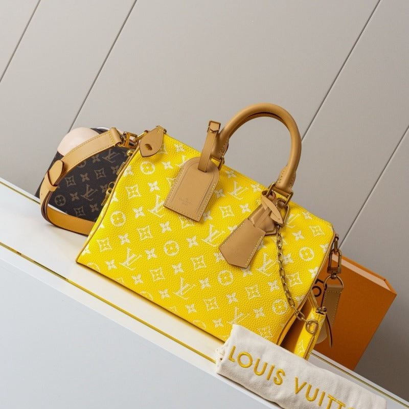 A Louis Vuitton yellow monogram handbag with tan leather handles and trim, displayed on a white shelf next to an orange box and a dust bag.