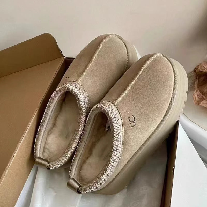 A pair of beige slip-on platform boots with a textured metallic trim around the collar, resting inside a brown cardboard box.