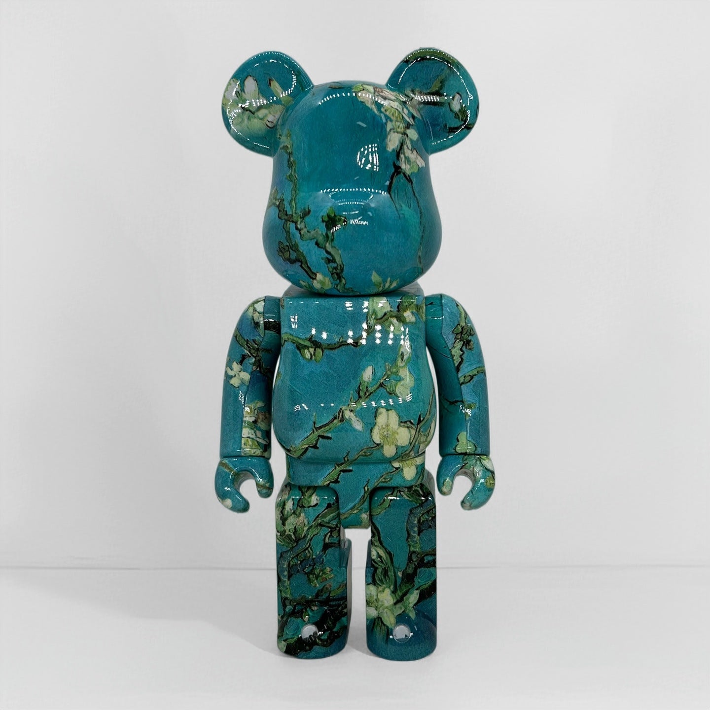 A glossy bear-shaped collectible figure with a teal and green floral branch print, standing against a plain light gray background.