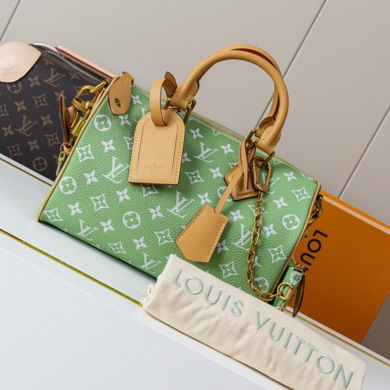 A green Louis Vuitton monogram Speedy handbag with tan leather handles and a gold chain strap, displayed on a white surface with a Louis Vuitton dust bag and orange box in the foreground.