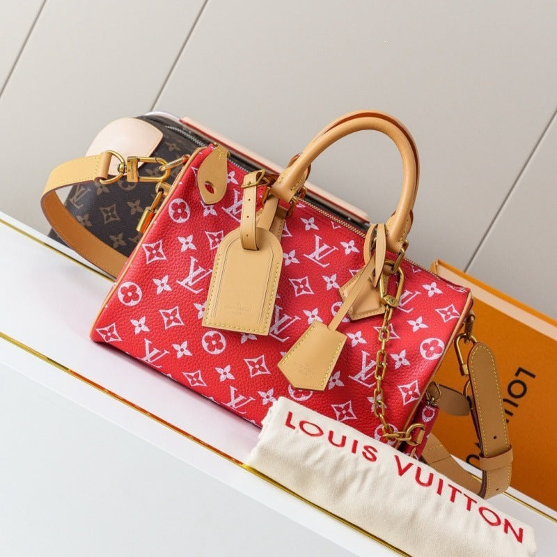 A Louis Vuitton red monogram Speedy handbag with tan leather handles and a gold chain strap, displayed on a white shelf alongside an orange Louis Vuitton box and a dust bag.