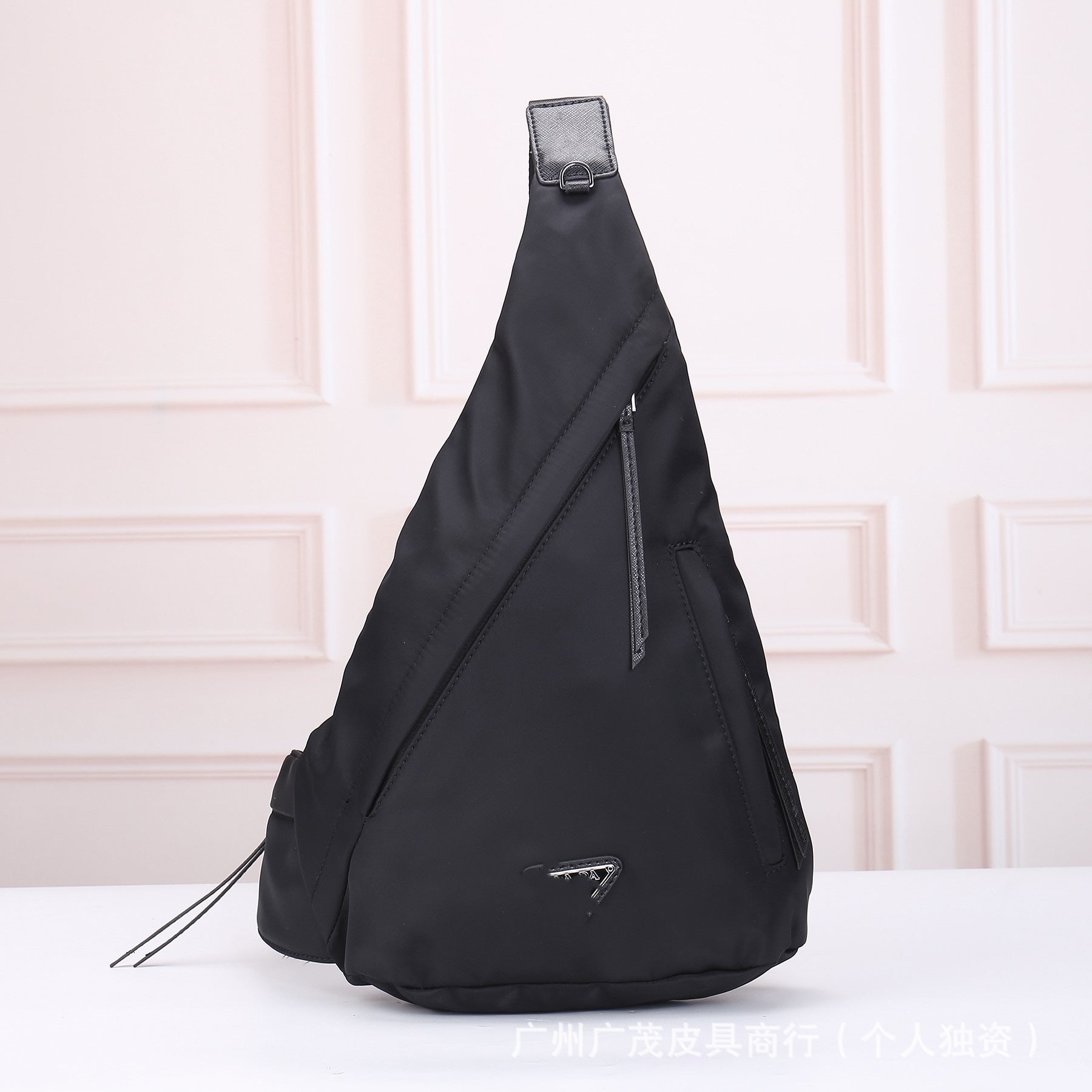 Black sling bag with a brand logo on a light pink background
