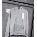Gray hoodie with a tag on a hanger against a reflective glass wall.