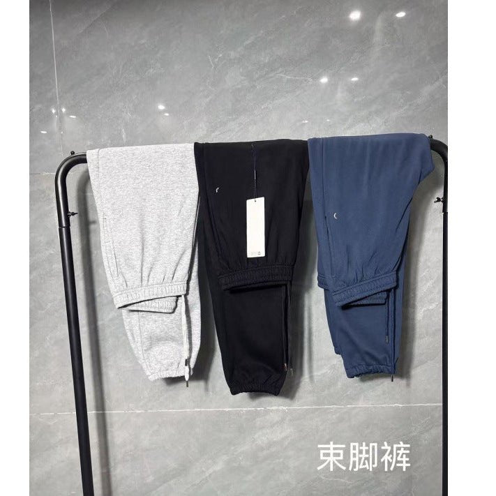 Three pairs of pants in gray, black, and blue hanging on a rack against a gray tiled wall.