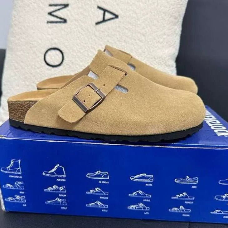 Tan clogs with a brown buckle on a blue box with brand logo