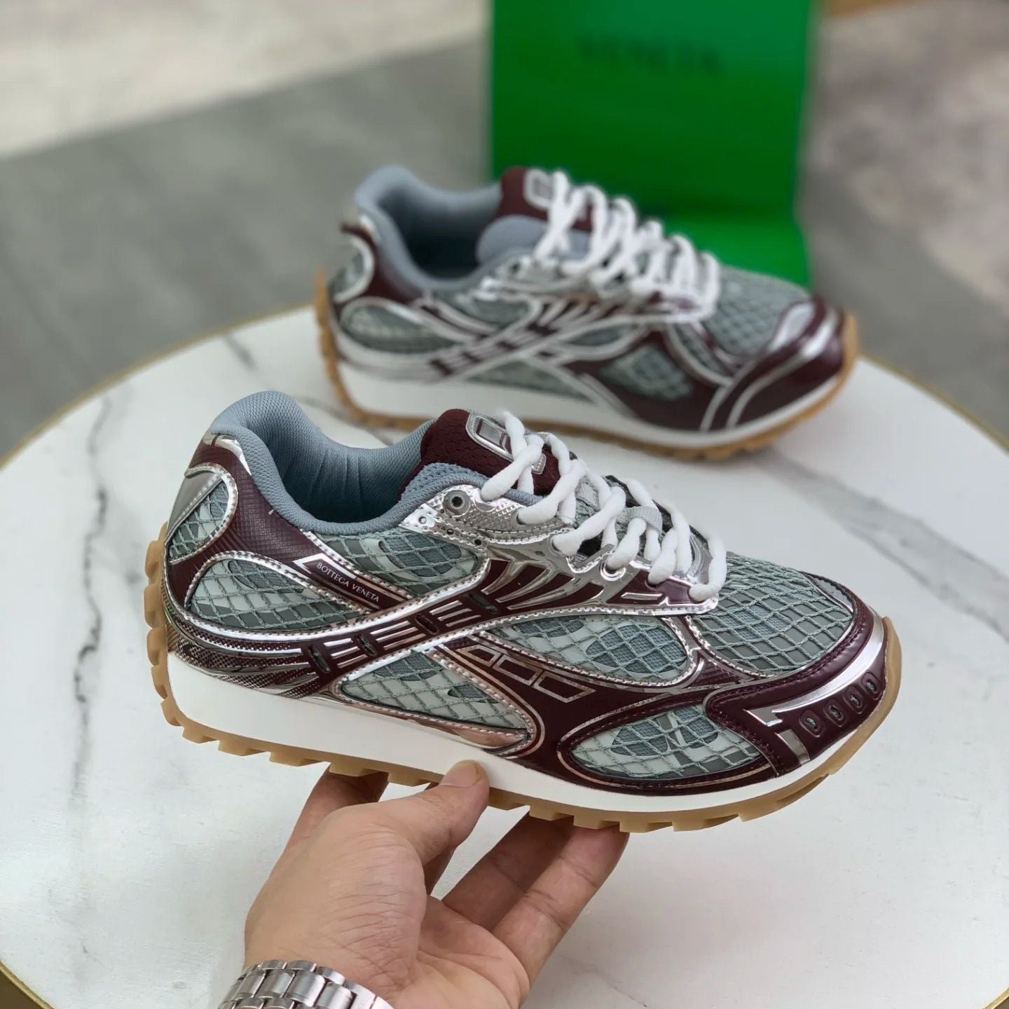 Maroon and gray sneakers with white laces on a marble surface.