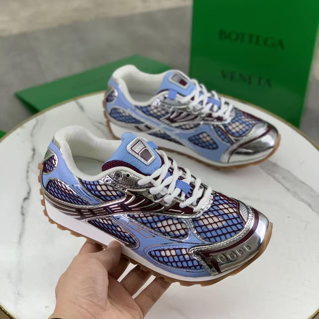 Colorful sneakers with a patterned sole held by a hand, with a green box in the background.