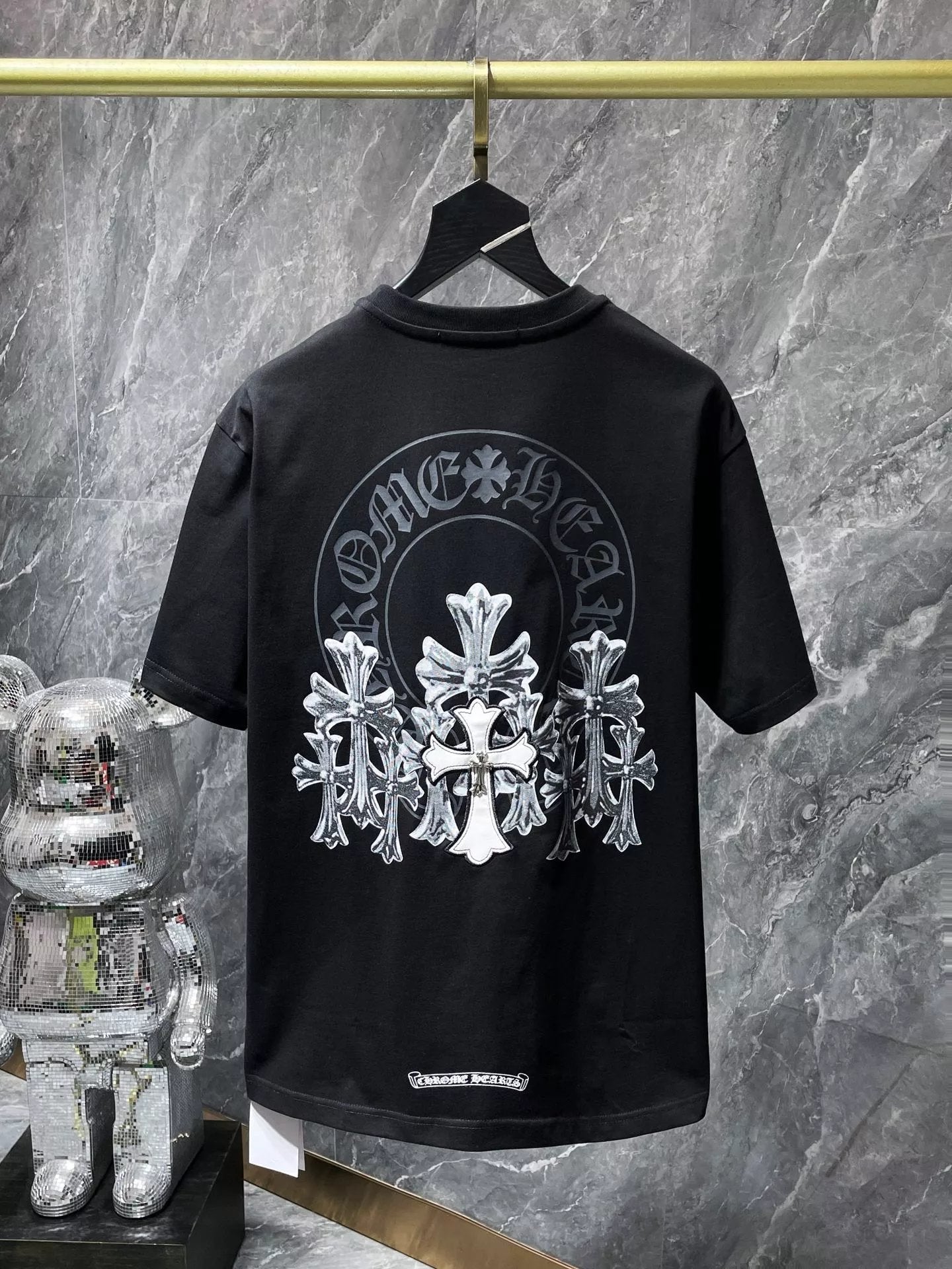 Black t-shirt with white graphic design on a hanger against a marble wall.